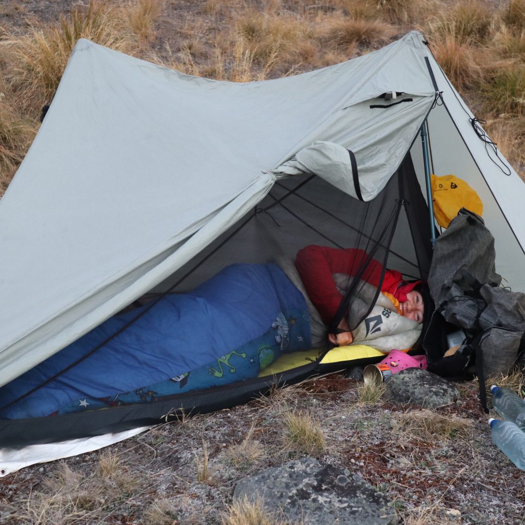 Ellie lying inside her sleeping back inside her ultralight tent whilst on trail. She is smiling.