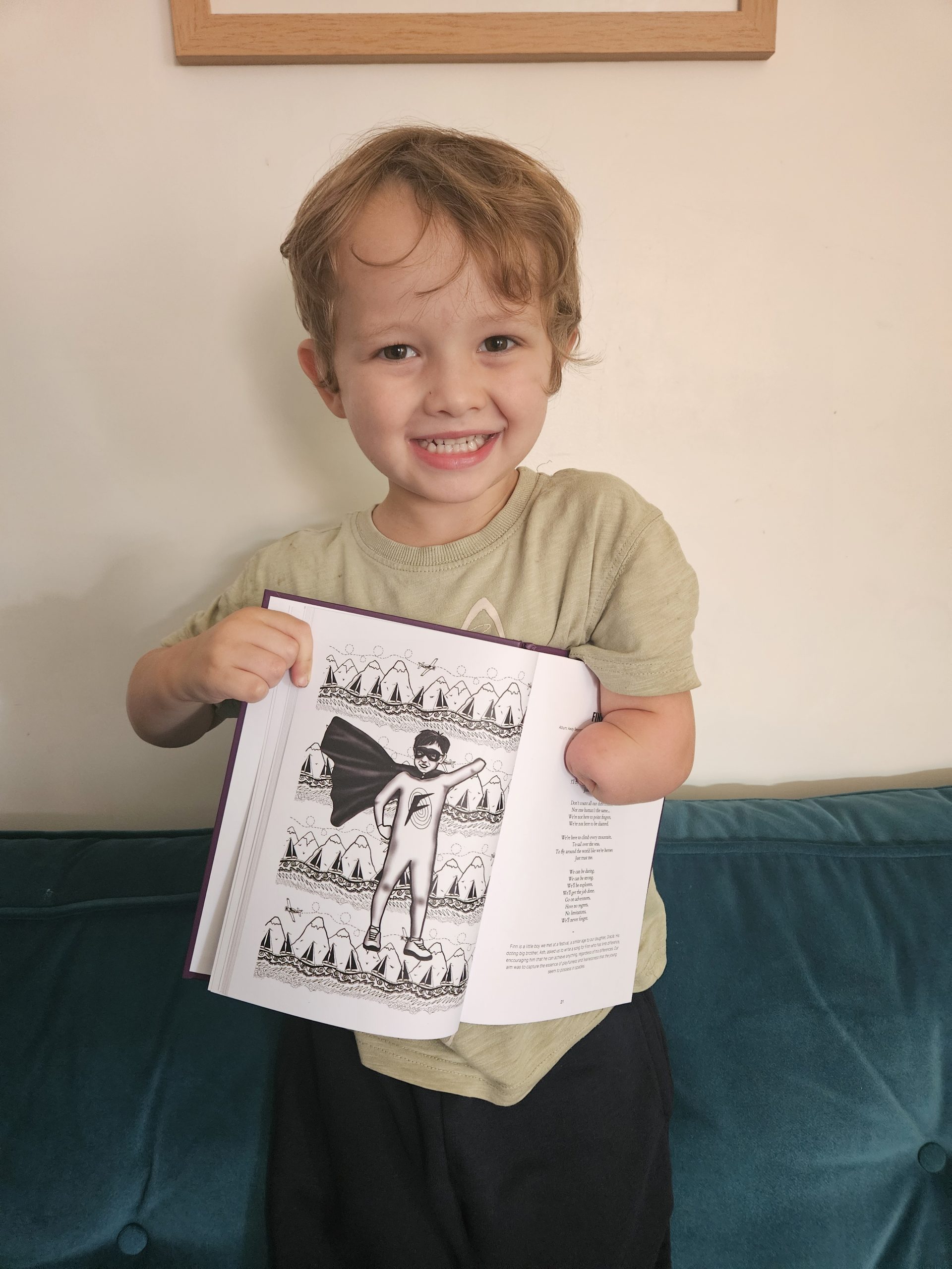 Finn smiling at the camera whilst holding the lyric book with his illustration in.