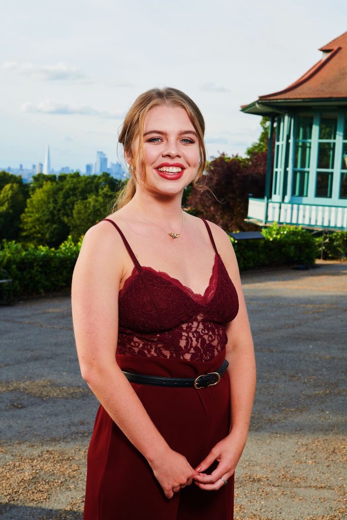 Lily poses for the camera, smiling in a burgundy dress for the dating show. 