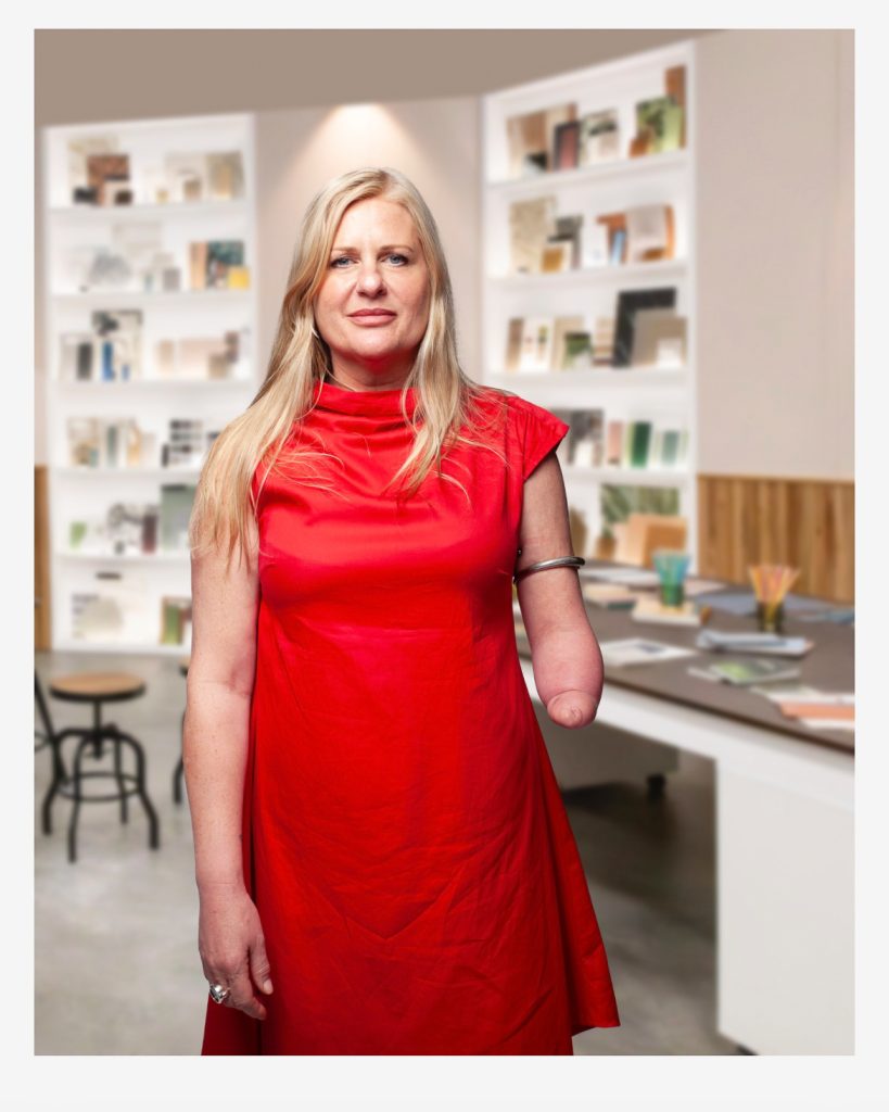 Emma stands confidently looking at the camera in a red dress as part of the Interior Design Masters promotional shots.