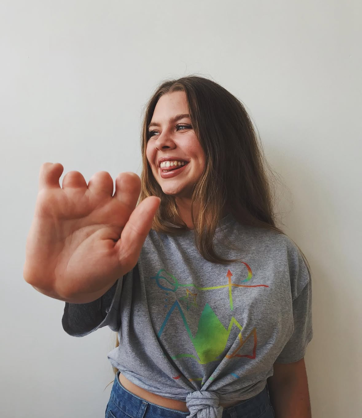 Lily holds her hand to the camera, she is smiling and looking away from the camera.